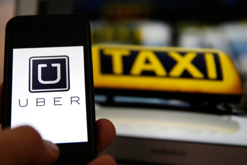 File illustration picture showing the logo of car-sharing service app Uber on a smartphone next to the picture of an official German taxi sign in Frankfurt, September 15, 2014. A Frankfurt court earlier this month instituted a temporary injunction against Uber from offering car-sharing services across Germany. San Francisco-based Uber, which allows users to summon taxi-like services on their smartphones, offers two main services, Uber, its classic low-cost, limousine pick-up service, and Uberpop, a newer ride-sharing service, which connects private drivers to passengers - an established practice in Germany that nonetheless operates in a legal grey area of rules governing commercial transportation.    REUTERS/Kai Pfaffenbach/Files  (GERMANY - Tags: BUSINESS EMPLOYMENT CRIME LAW TRANSPORT)